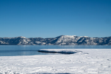 Frozen shore of Lake Tahoe in the winter, featuring cloudless blue sky and water copy-space, near Tahoe City, California side