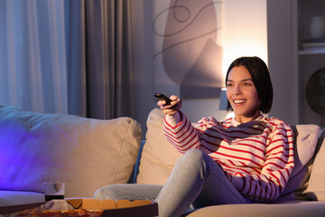 Happy woman watching TV with pizza on sofa at home, space for text
