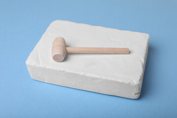Educational toy for motor skills development. Excavation kit (plaster and wooden mallet) on light blue background, closeup