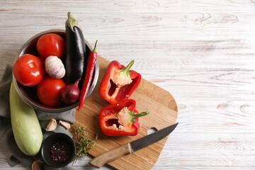 Cooking delicious ratatouille. Fresh ripe vegetables, knife and bowl on white wooden table, flat lay. Space for text
