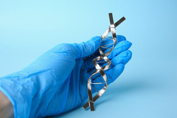 Scientist with DNA molecular chain model made of metal on light blue background, closeup