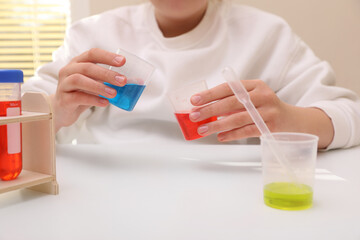 Girl mixing colorful liquids at white table indoors, closeup. Chemical experiment set for kids