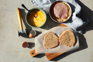 Cooking schnitzel. Raw pork chops in bread crumbs, meat mallet and ingredients on grey table, flat lay