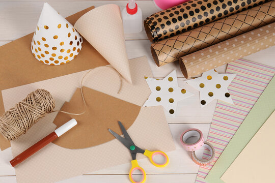 Stationery and different materials to create party hats on white wooden table, flat lay. Handmade decoration