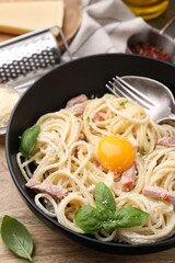 Bowl of delicious pasta Carbonara with egg yolk on wooden table, closeup
