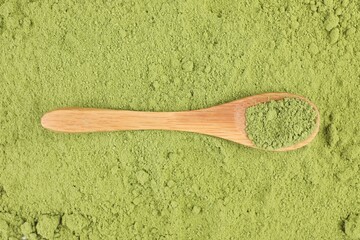 Wooden spoon on green matcha powder, top view