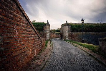 A paved road inside the brick walls of an ancient castle. Stone road among the brick walls of the old fort, overgrown with green grass