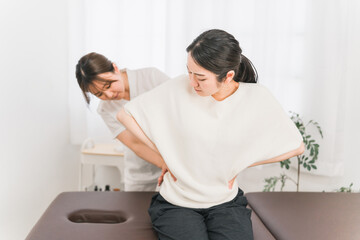 整体院・整骨院に腰痛の治療にきた患者と整体師・マッサージ師・セラピスト・医師の女性
