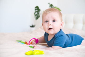 baby boy in blue bodysuit playing with colorful plastic toys on bed