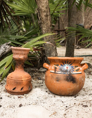 Hand made ceramic pot in sandy tropical garden with green palm leaves on a sunny day in Tulum 