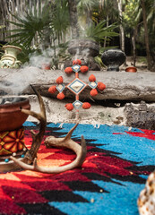 Sacred Maya ceremony objects with incense burner and Red Cross  in a tropical sandy garden surrounded by green plant 