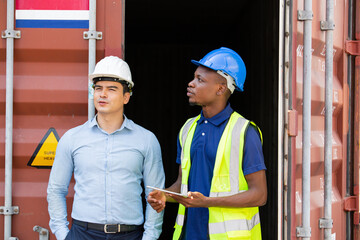 Logistic foreman discussing business work with African contractor worker at container warehouse or construction site.