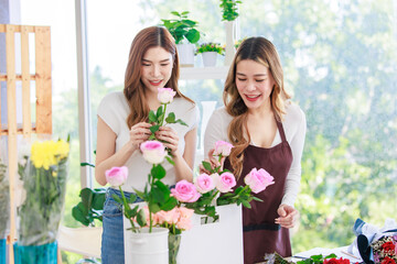 Asian professional successful female florist designer flower shop owner entrepreneur and colleague employee helping decorating pink roses bouquet in floral garden store studio
