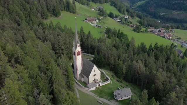 Aerial drone view of an old secluded mountain top church in the Italian alps surrounded by a forrest of trees 06