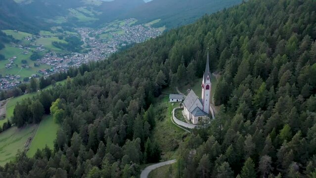 Aerial drone view of an old secluded mountain top church in the Italian alps surrounded by a forrest of trees 05