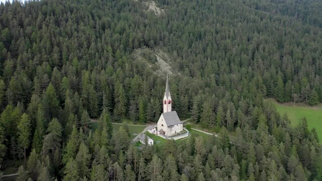 Aerial drone view of an old secluded mountain top church in the Italian alps surrounded by a forrest of trees 02
