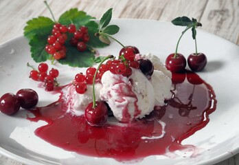 Red cherries and red currants on ice cream with jam in a white plate on a white wooden table.Food background.