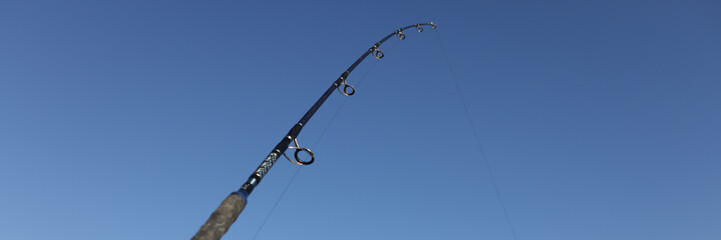 Obraz premium Fishing rod on sea beach on blue sky background