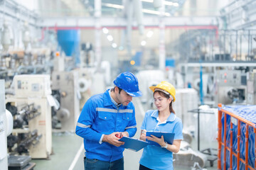 Half body photo of American male engineer and female manager Watching listnotes and meeting holding a radio Wear a helmet and uniform. in the plastic and steel industry There is a working machine