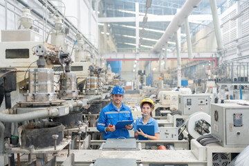 American male engineer and female manager In the center of the picture, surrounded by working machines. holding a list note and a radio Wear a helmet and uniform. in large plastic and steel factories