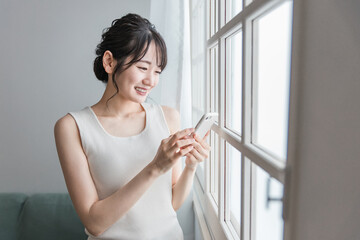 家でスマホを使う笑顔のアジア人女性（SNS・動画・ゲーム）
