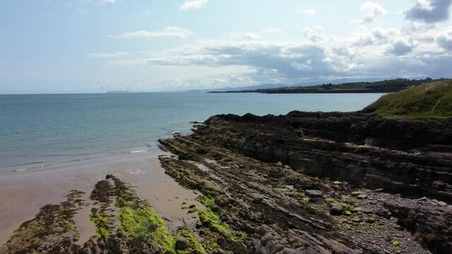 Aerial view Traeth Lligwy Jurassic rocky weathered rugged Anglesey coastal shoreline, push in shot towards ocean