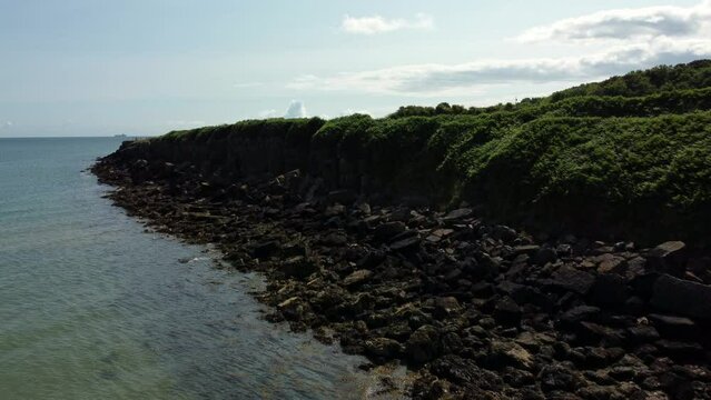 Aerial view Traeth Lligwy Jurassic rocky weathered rugged Anglesey coastal shoreline, rising shot