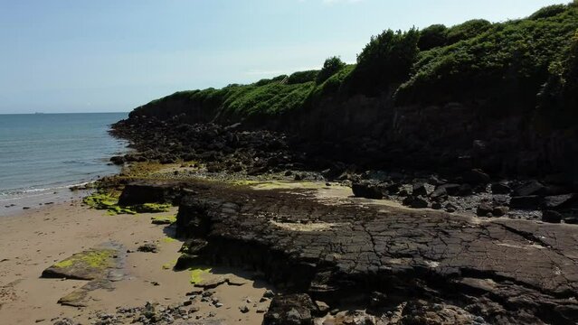 Aerial view Traeth Lligwy Jurassic rocky weathered rugged Anglesey coastal formation, low forward push in