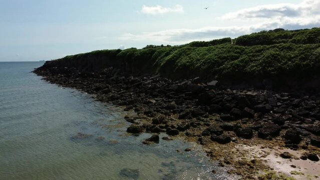 Aerial view Traeth Lligwy Jurassic rocky weathered rugged Anglesey coastal shoreline, slow push in