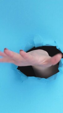 Vertical video. So-so gesture. Not sure. Skeptic doubt. Female hand waving inside breakthrough paper hole on blue torn wall background with free space.