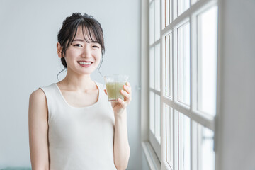家でグリーンスムージーを飲む笑顔のアジア人女性
