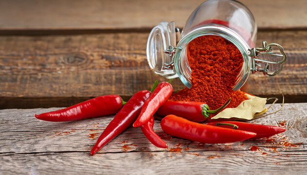 Ground hot red pepper in a glass jar and fresh chili peppers on old wooden background, selective focus