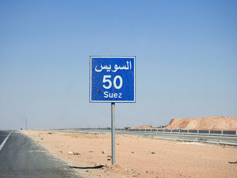 A road sign board in Suez Cairo highway gives the remaining distance to Suez city 50 KM fifty kilometers written in English and word Suez written in Arabic and English at the side of the street