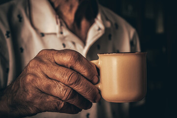 Closeup of unrecognizable aged person with wrinkles and veins holding mug of hot coffee in hand...