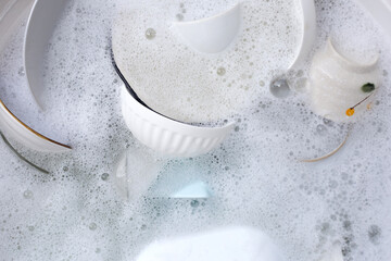 Dishes and bowls in water and bubbles of dishwashing liquid. Kitchen work