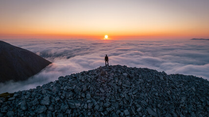 Hiker looking at the sunrise on top the clouds on a Scottish mountain, witnessing a cloud inversion...