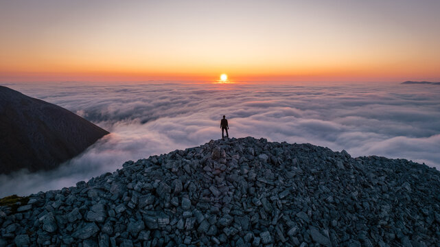 Hiker looking at the sunrise on top the clouds on a Scottish mountain, witnessing a cloud inversion over An Teallach.