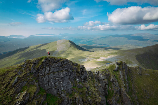 An aerial panorama capturing a hiker standing on a mountain ridge in the Scottish wilderness on a summers day.