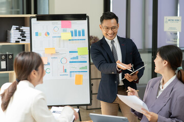 Asian business presents to explain the graph work on the whiteboard. Consulting, discussing, exchanging knowledge.