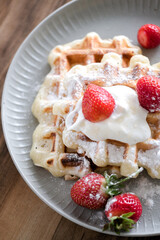 Belgian waffles with strawberry and powdered sugar on plate, wooden table background