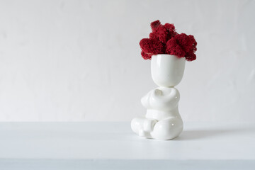 White ceramic figurine of human with colorful stabilized moss from head is sitting in lotus position