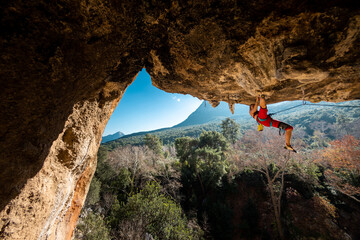 girl rock climber climbs a rock against the backdrop of a forest and blue mountains. climber goes...