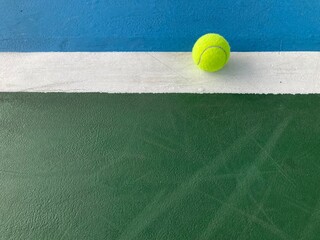 the green tennis ball is at the end of the white backline of a blue-green tennis court in daylight
