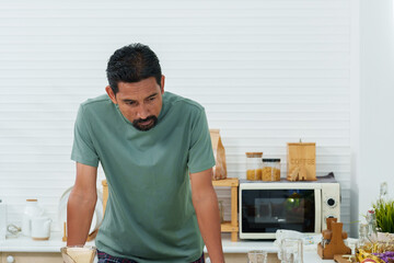 Asian man standing with his arms on the table in the kitchen preparing breakfast, thinking what to cook. in the morning of the holiday Before starting a work-at-home job