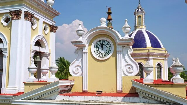 Hermosa toma de done que gira sobre el reloj de la parroquia San Cristobal de Asis y permite ver al fondo la cupula de la parroquia. Colima