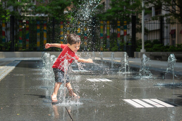 Young boy playing in a fountain at an urban spray park.
