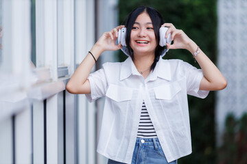 Happy of cute smiles Asian of attractive young Cute little girl wearing white wireless headphones and listening music enjoying favourite audio at the cafe on vacation at a coffee shop the park outdoor