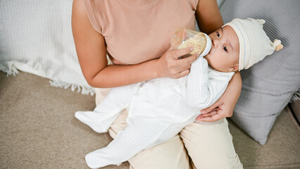 Portrait of cute newborn baby being fed by her mother using bottle.