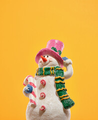 New year holiday figurine of a cheerful snowman with a pink hat and a green long scarf. The snowman is holding a sweet lollipop and smiling. Festive mood and gift time.