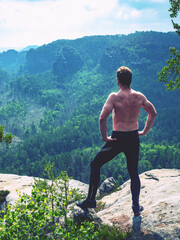 Half naked man hold arms as akimbo at end of rocky cliff.